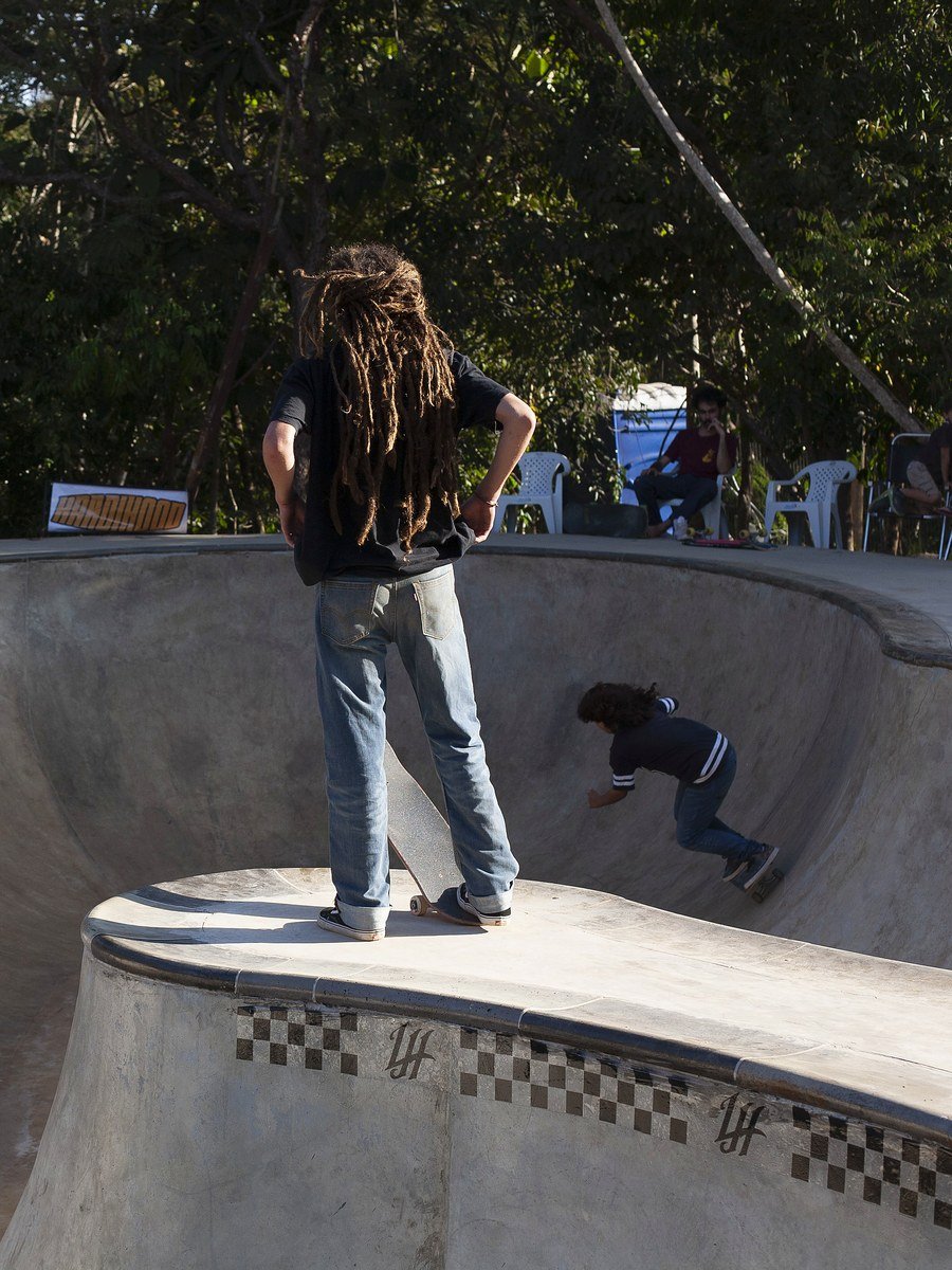 Skatista parado no coping observando a linha de quem está andando dentro do bowl