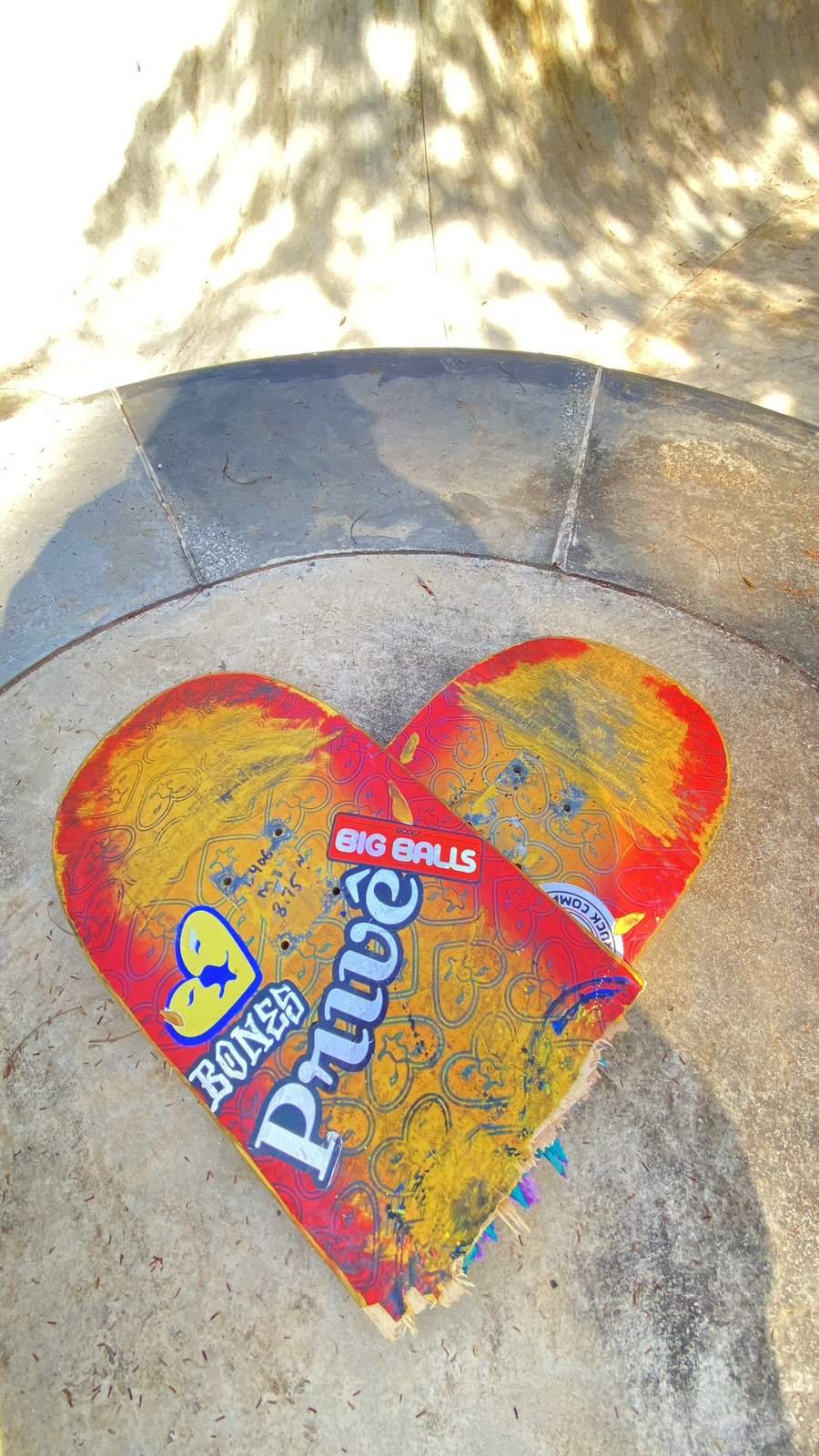 Shape de skate usado, com pintura desgastada, apoiado no coping do bowl